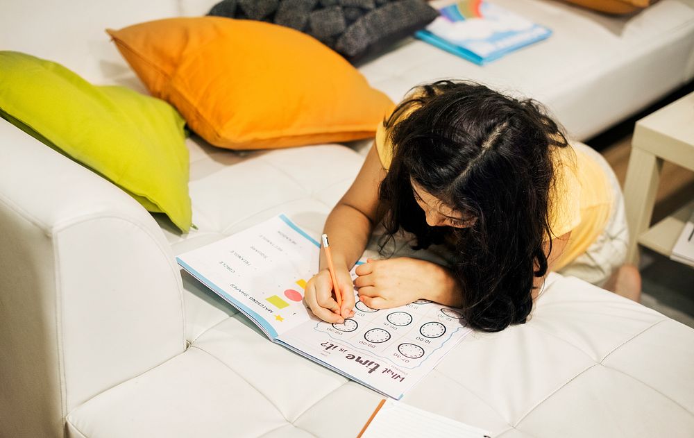 Young girl working on exercise book on couch