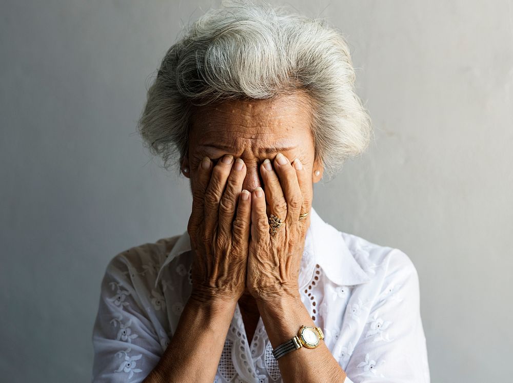 Elderly Asian woman with hands covered her face