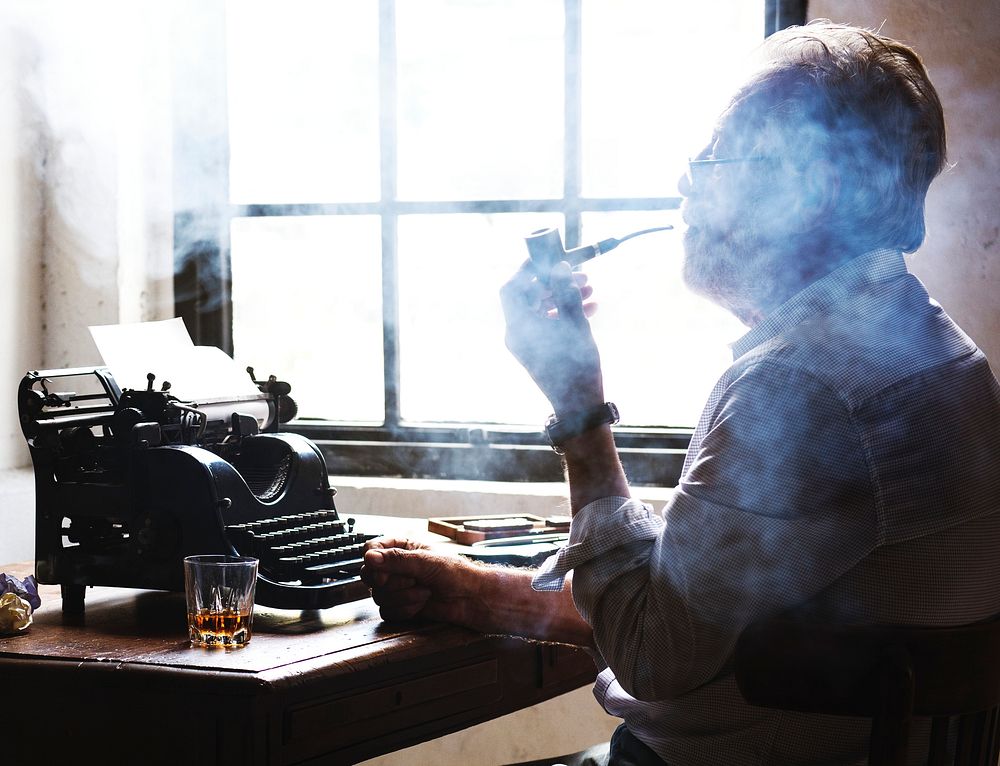 Side view of man smoking pipe while working on typewriter