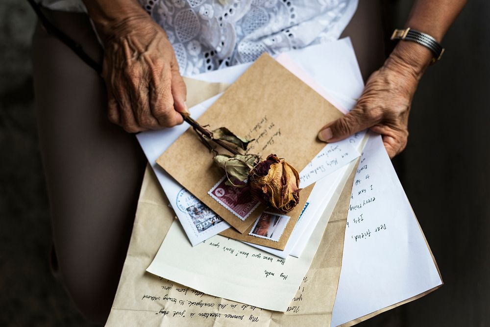 Elderly woman holding old letters and dried rose