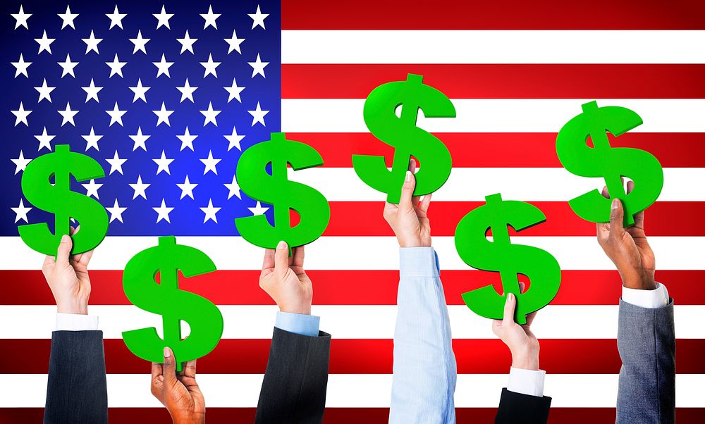 Multi-Ethnic Hands Holding Dollar Signs With Flag Of USA For The Background.