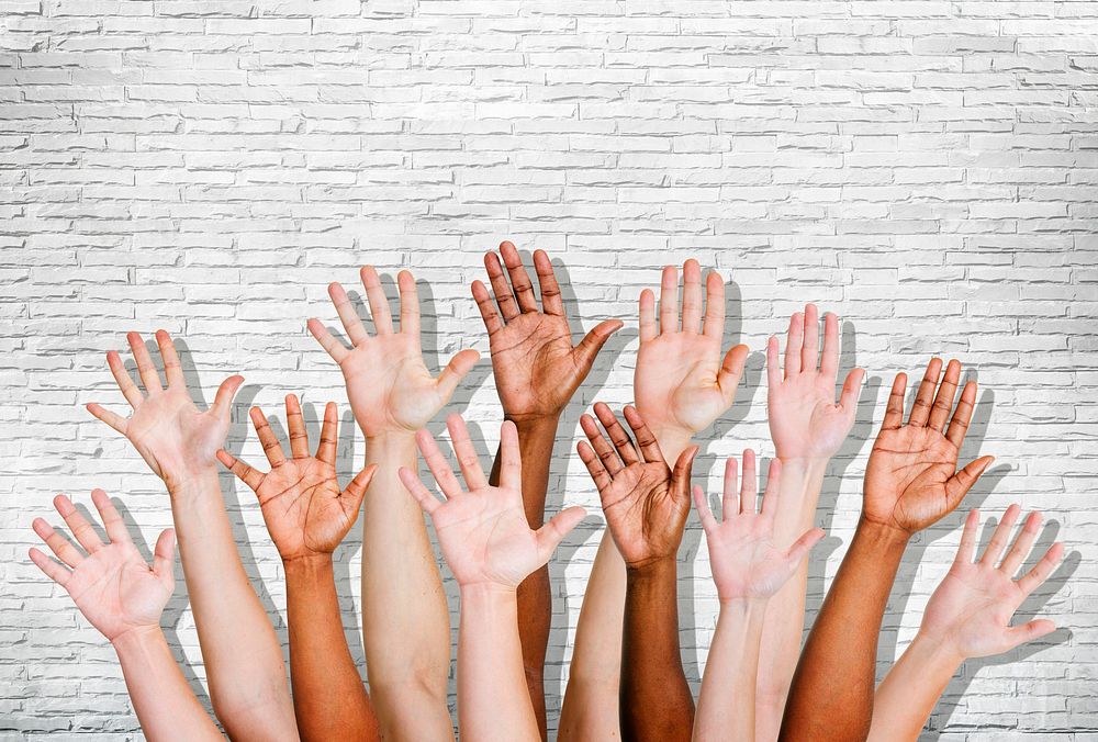 Group of human arms raised with brick wall.