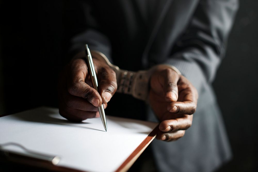 Closeup of hands cuffed forced to sign paper