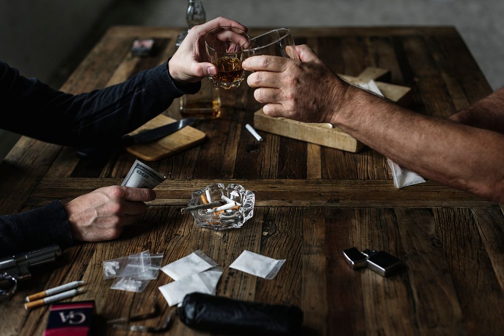 Hands doing a toast with drug paraphernalia on the table