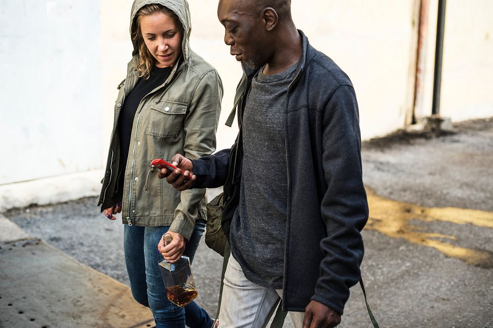Two people walking with a mobile and a bottle of alcohol