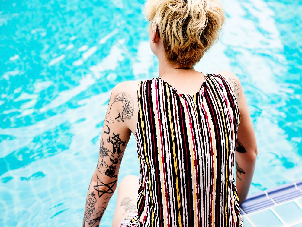 Rear view of caucasian tattooed woman sitting by the pool