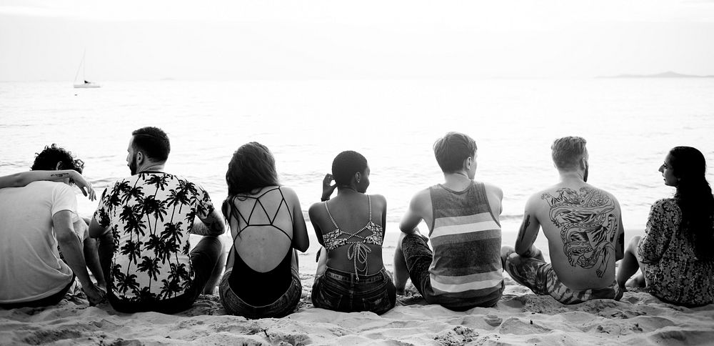 Rear view of diverse friends sitting at the beach together