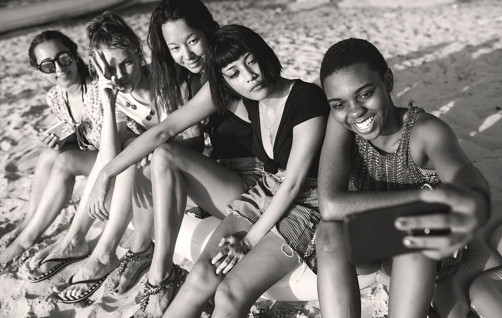 Group of diverse women sitting at the beach taking selfie together