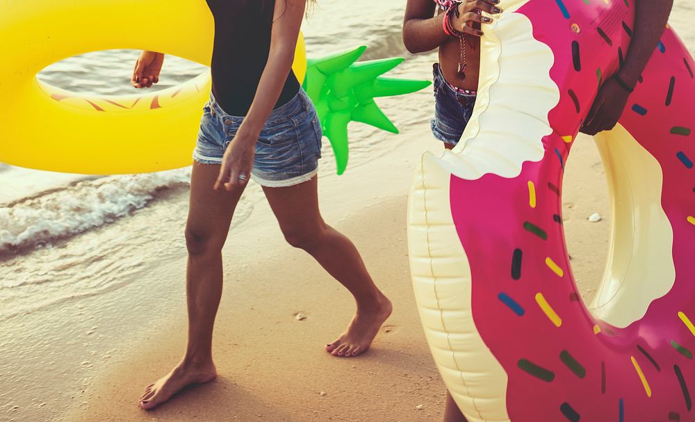 Diverse women walking at the beach with inflatable tubes