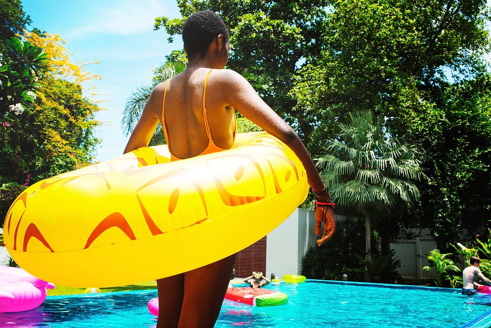 African woman standing by the pool with inflatable tube enjoying summer time