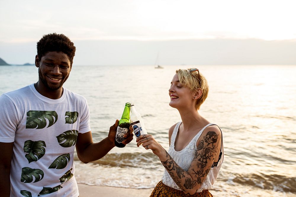 Caucasian woman clinking beer bottle with black man at the beach
