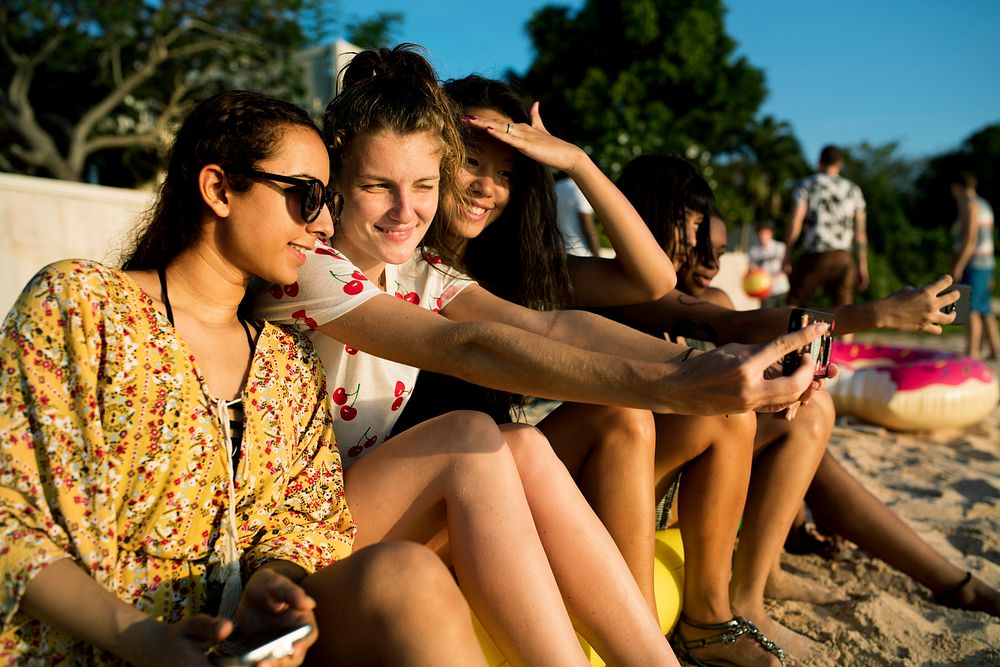 Group of diverse women sitting at the beach taking selfie together