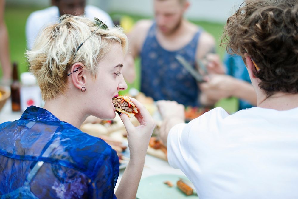 Closeup of a Caucasian woman eating burger at a meal with friends