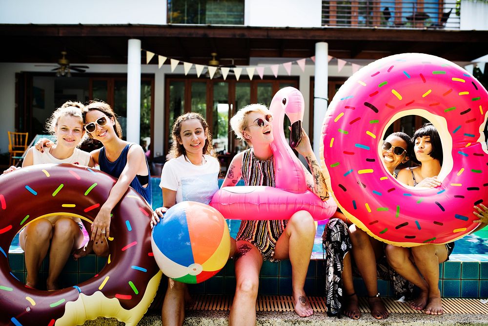Group of diverse women sitting by the pool with inflatable tubes