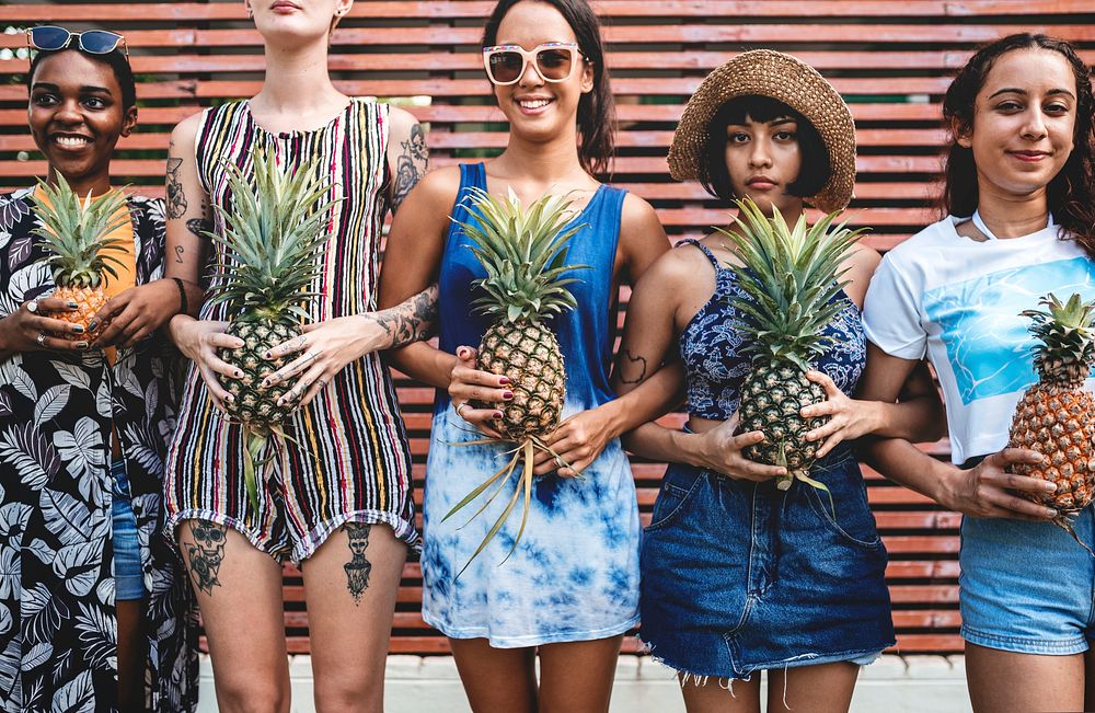 A diverse group of women standing and holding pineapple together