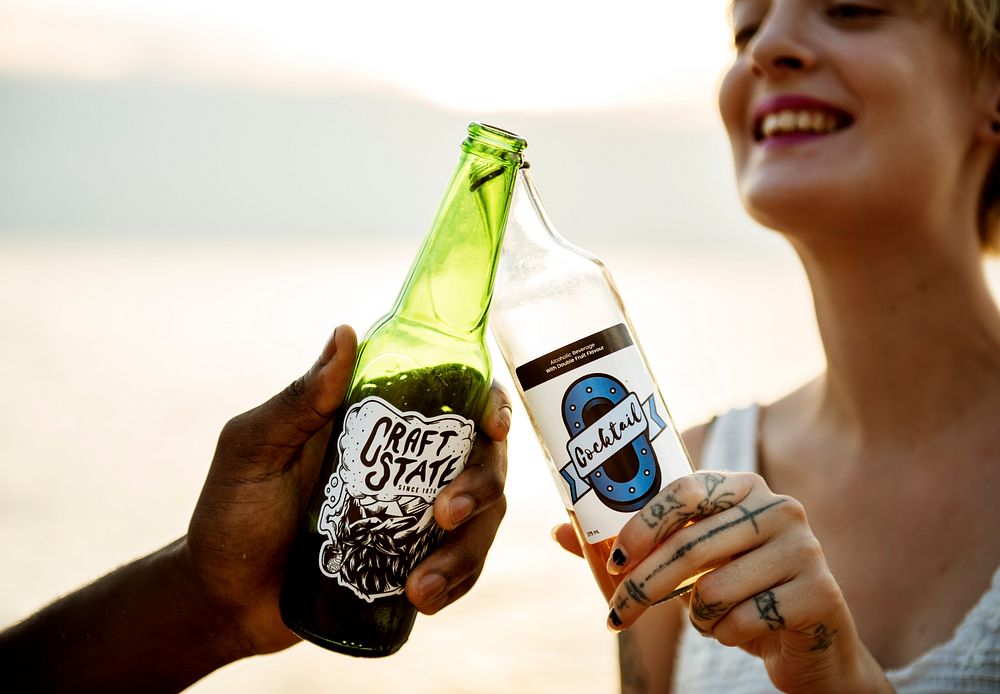 Clsoeup of caucasian woman clinking beer bottle with black man at the beach