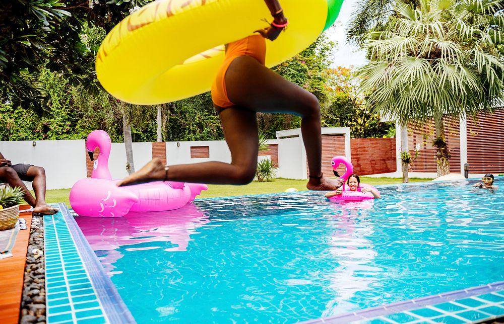 An African woman jumping into the pool with inflatable float and enjoying summer time