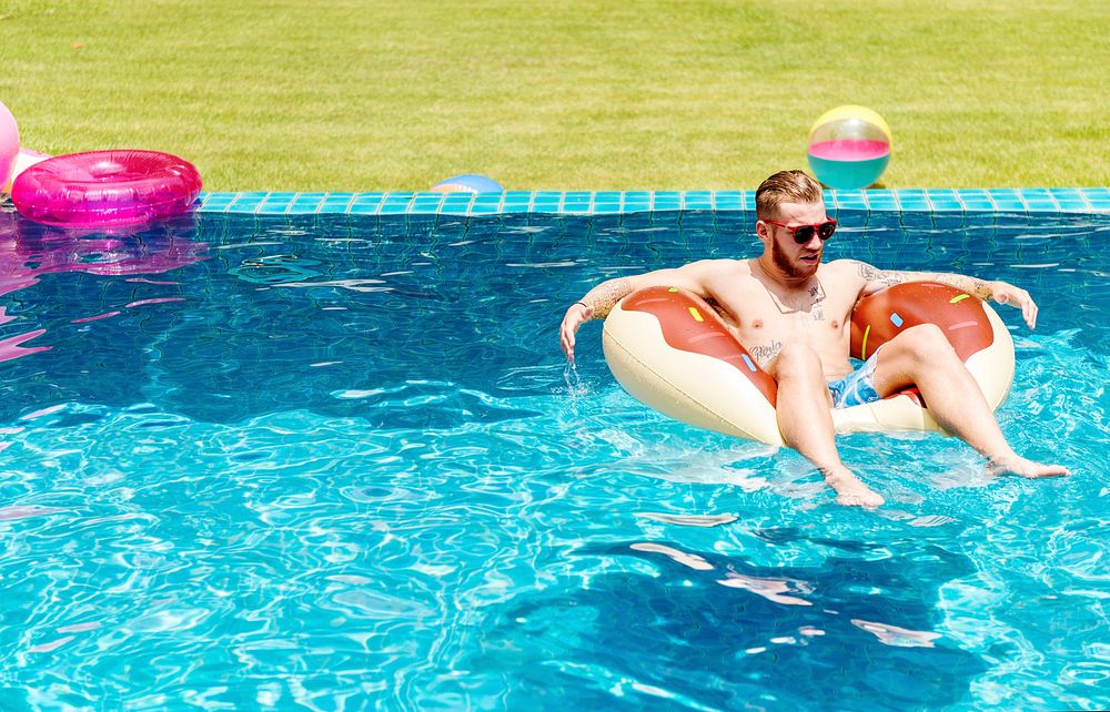 A Caucasian tattooed man on an inflatable float in the swimming pool