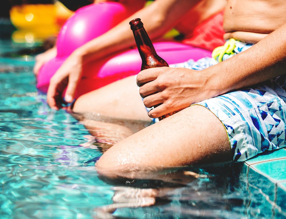 Closeup of man hand holding a beer bottle by the pool side