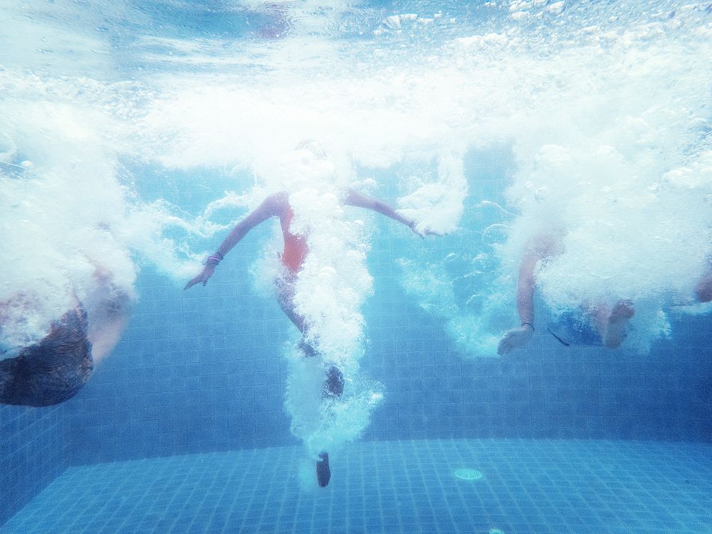 An underwater shot of a group of people jumping down into a swimming pool 