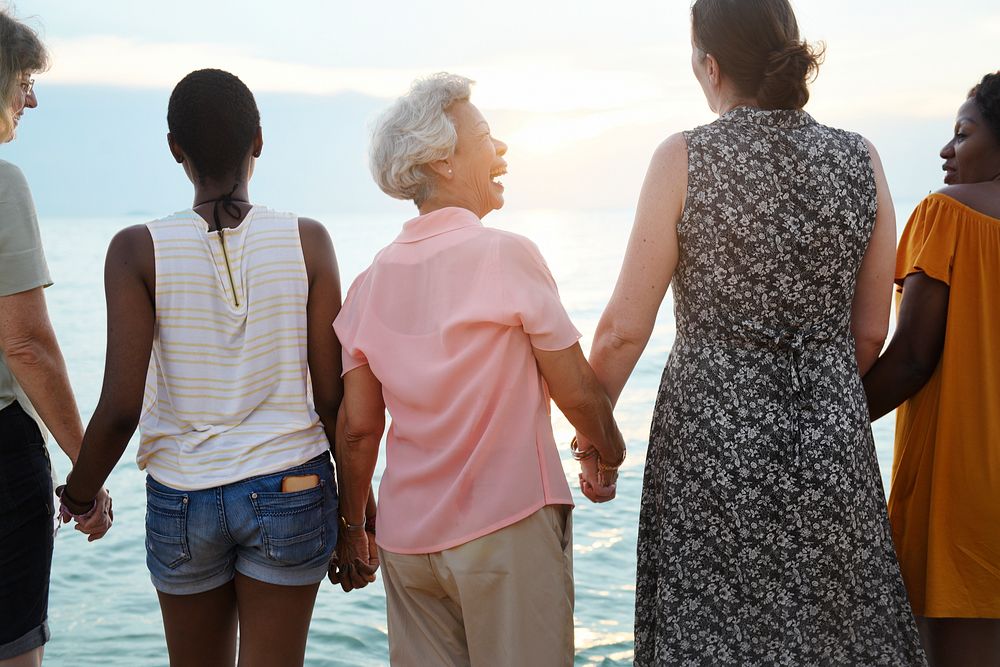 Rear view of diverse senior women holding hands together at the beach