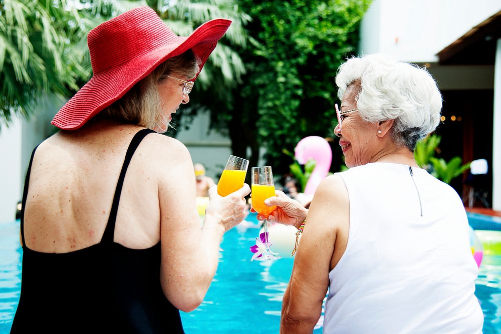 Senior couple women with orange juice by the pool together