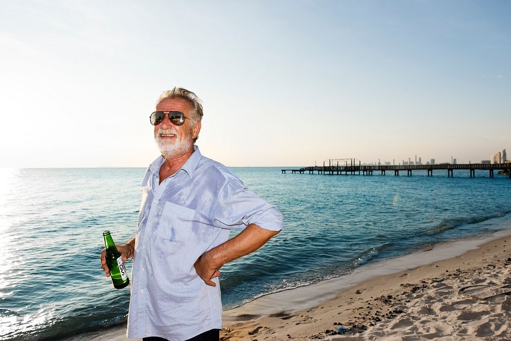 Cheerful senior adult with beer standing on the beach