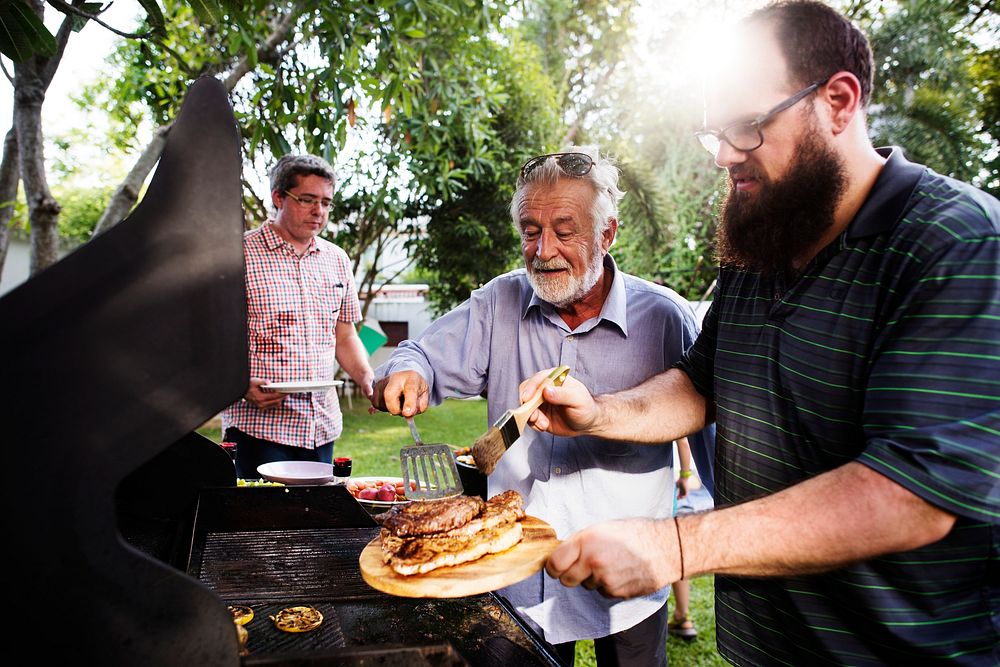 Men helping cooking homemade steak at bakcyard summer party