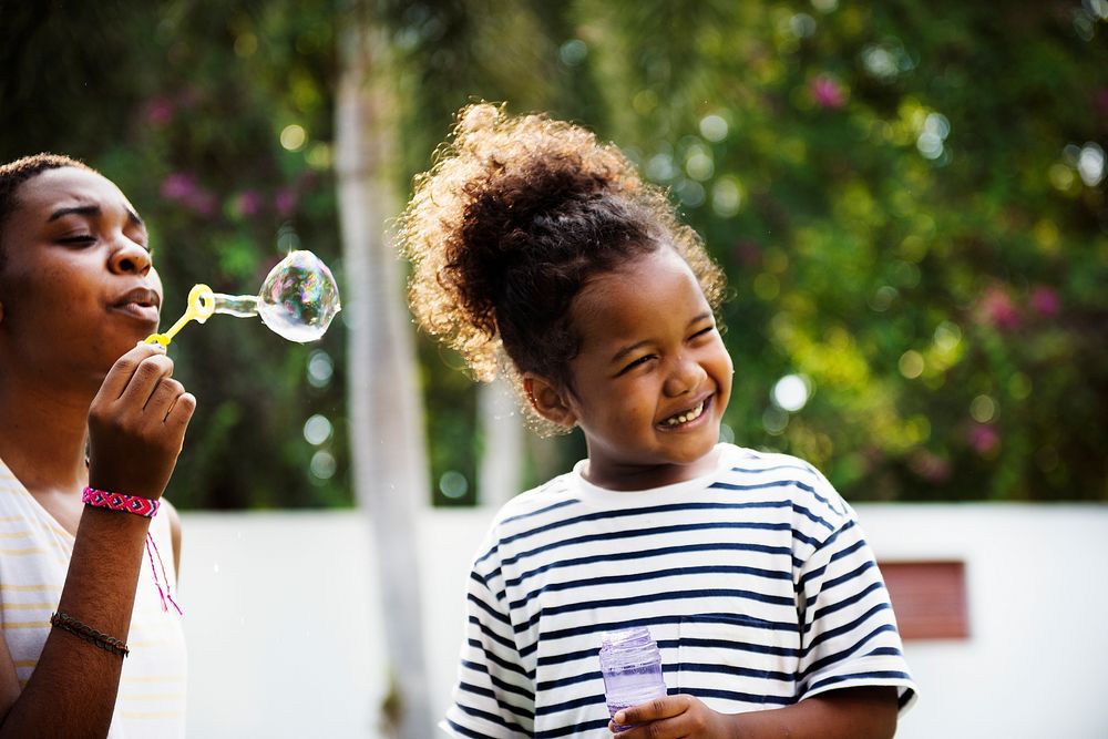 Black family enjoying summer together at backyard blowing soap bubbles