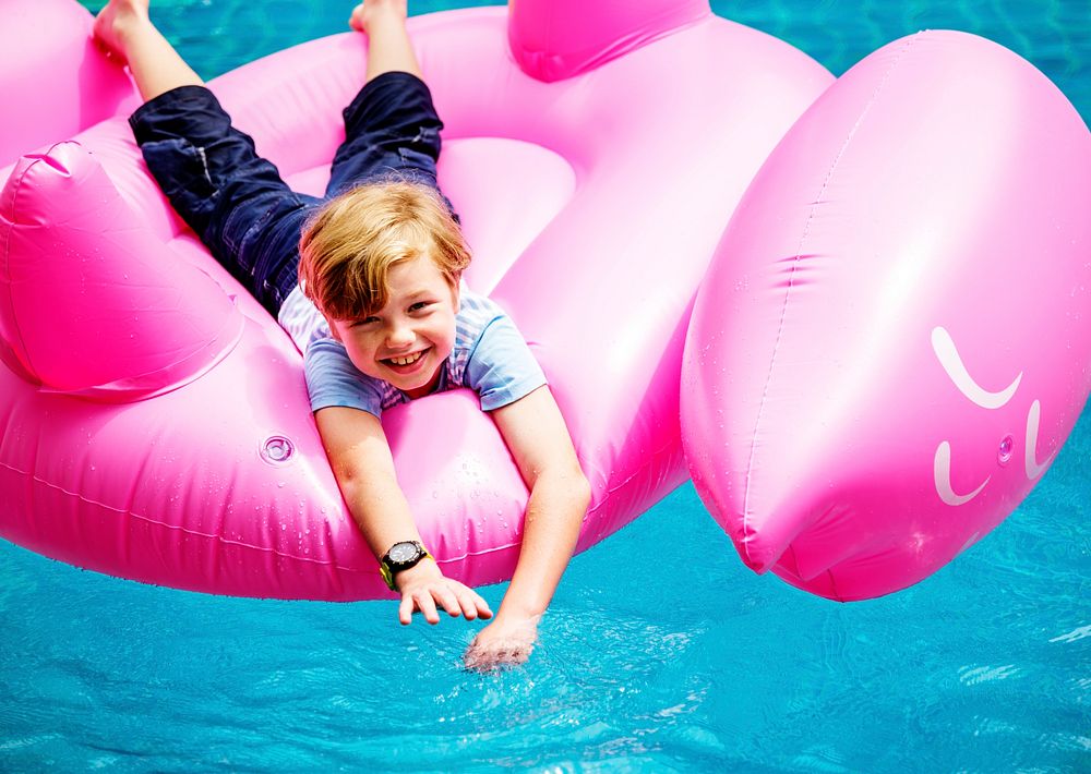 Aerial view of young caucasain boy floating in the pool with flamingo shape inflatable tube