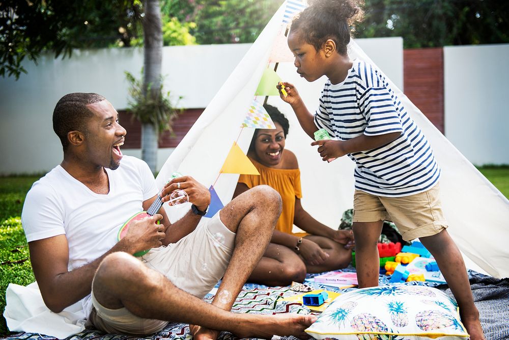 Black family enjoying summer together at backyard blowing soap bubbles