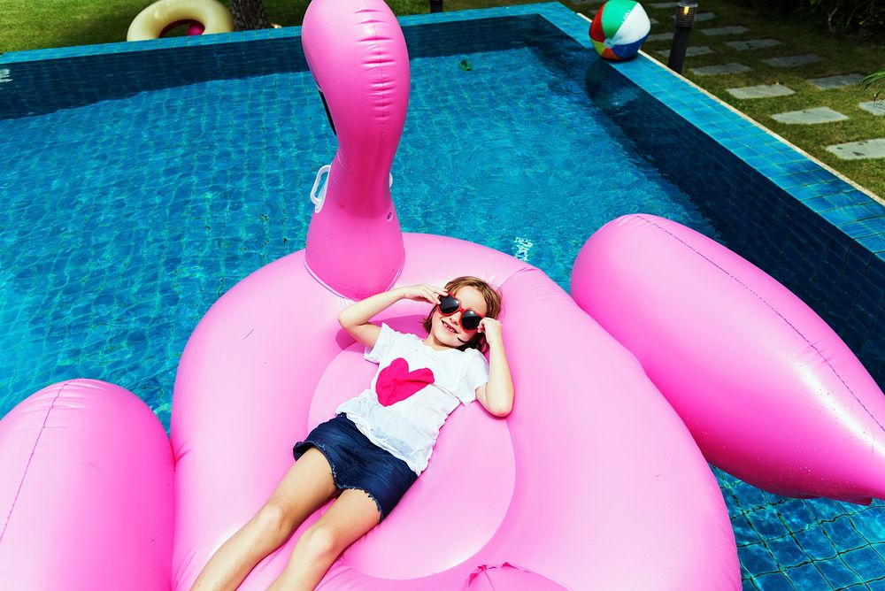 Aerial view of young caucasian girl floating in the pool with flamingo shape inflatable tube