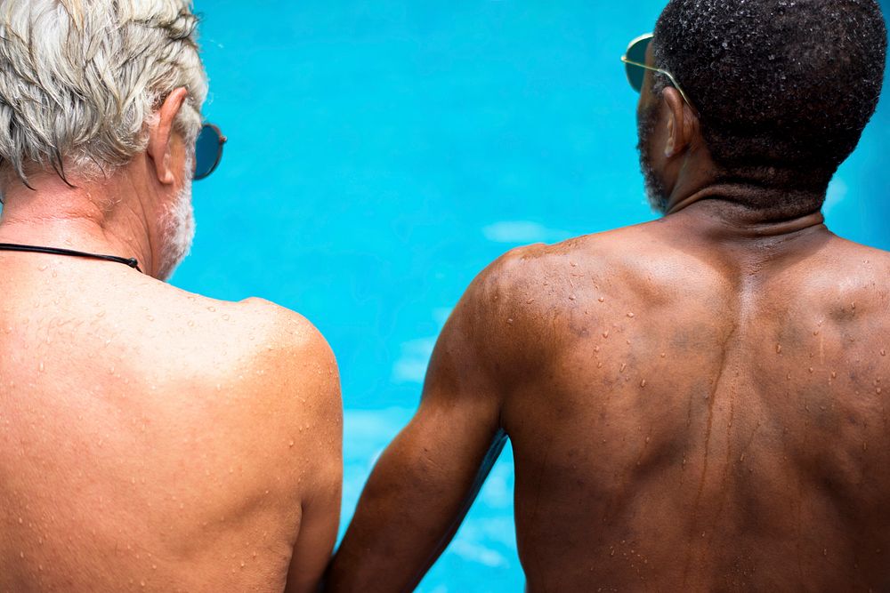 Rear view of diverse senior adults sitting by the pool enjoying summer together