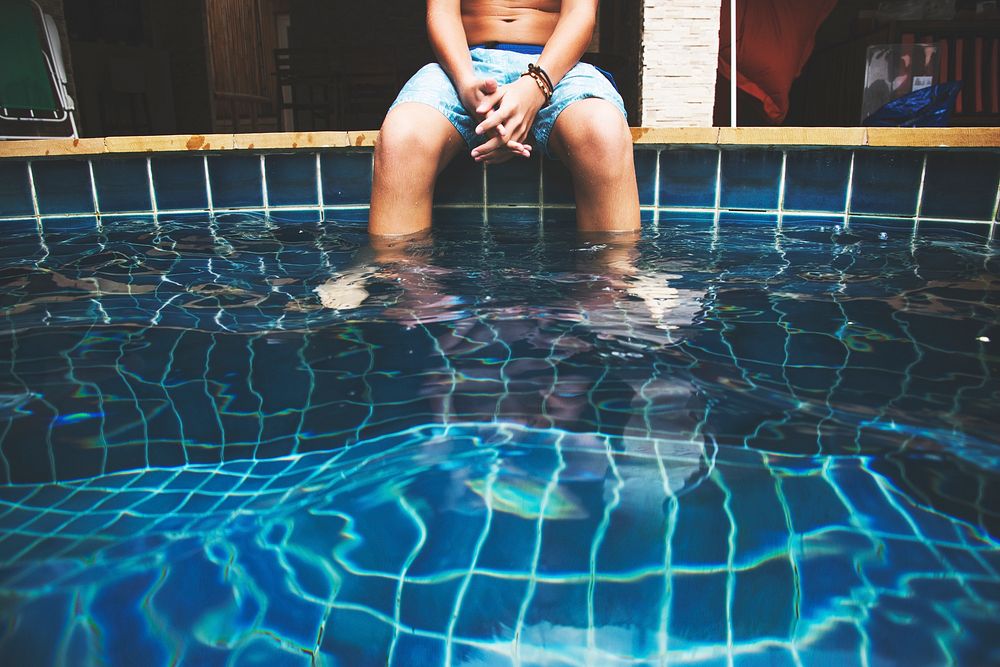 Young caucasian boy put feet in swimming pool