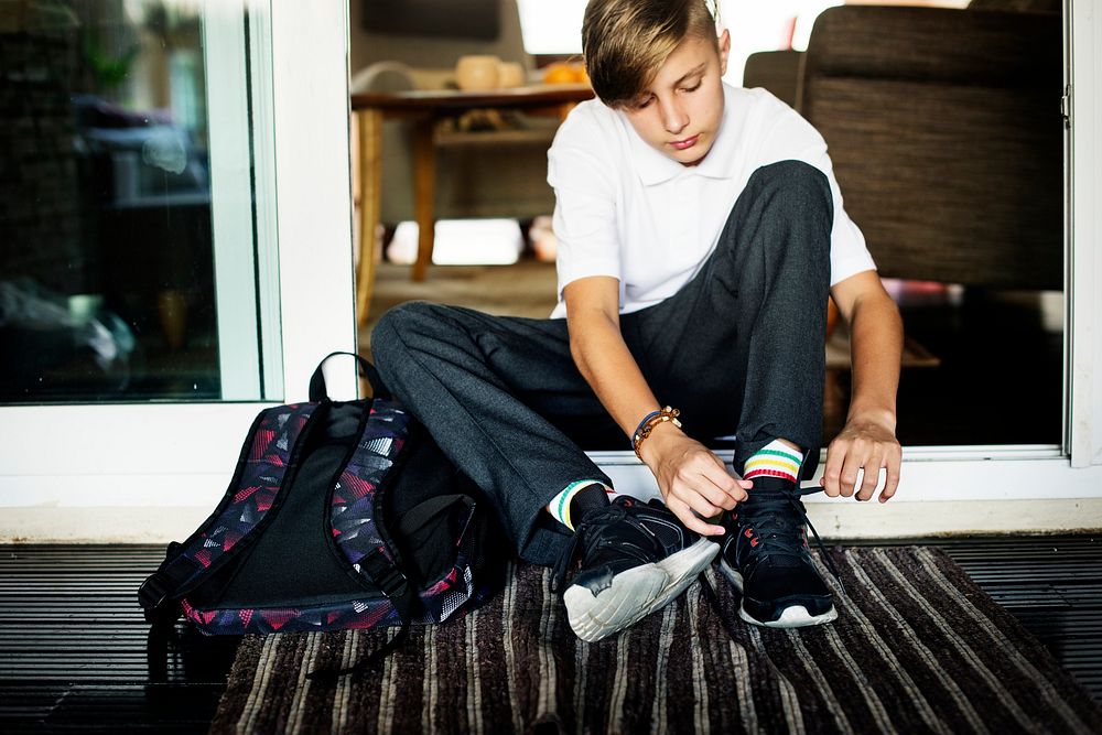 Young caucasian boy sitting on the house entrance tying sneaker ropes