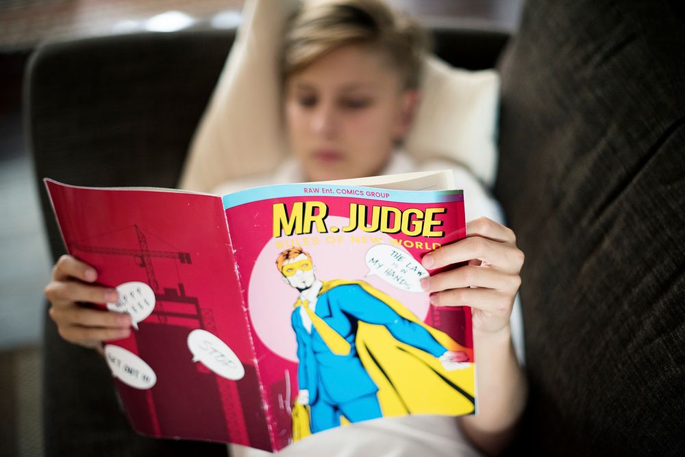 Young caucasian man lying on the couch reading comics