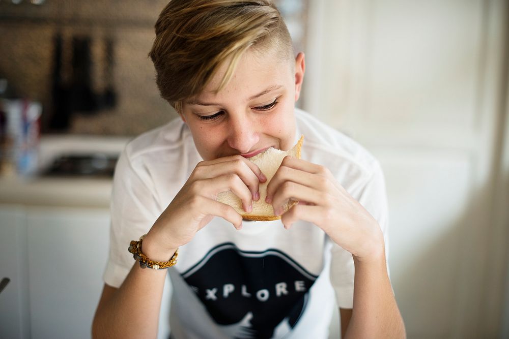 Young caucasian man eating sandwich in kitchen