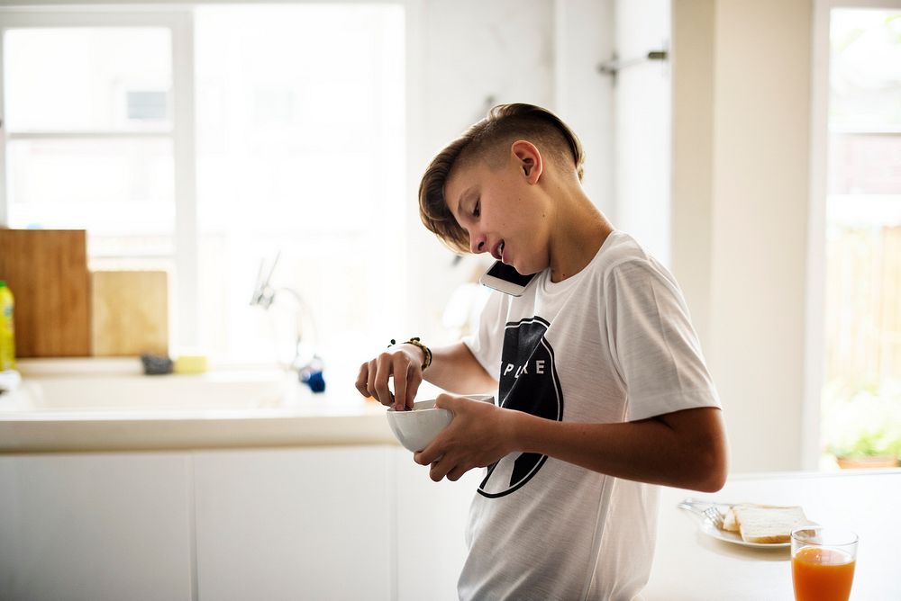 Closeup of young caucasain boy holding cereal bowl while talking on the phone in the kitchen