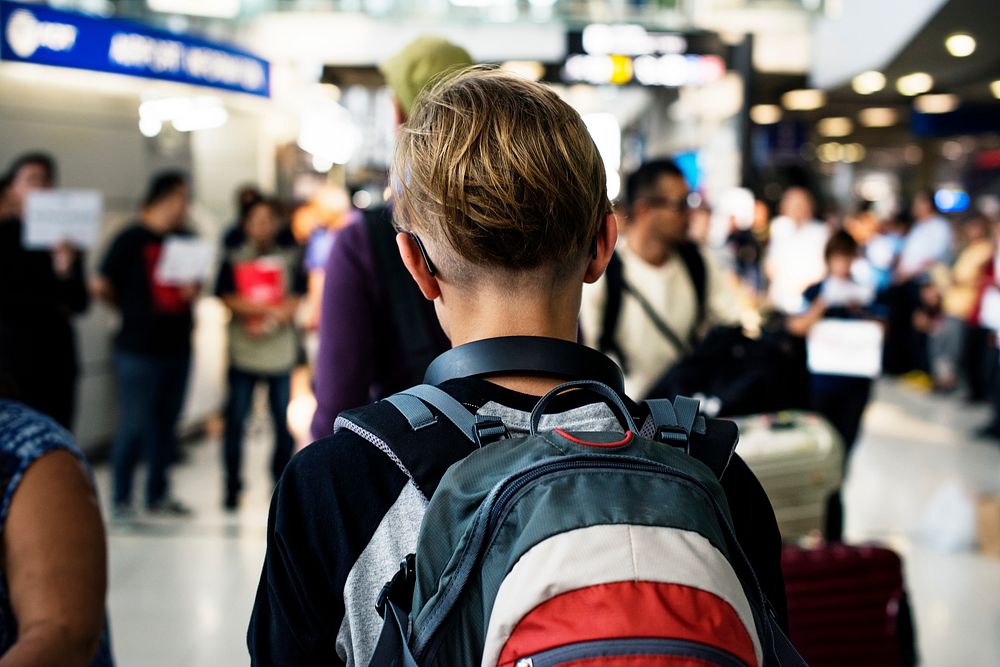 Rear view of young caucasian boy walking in the crowded at airport