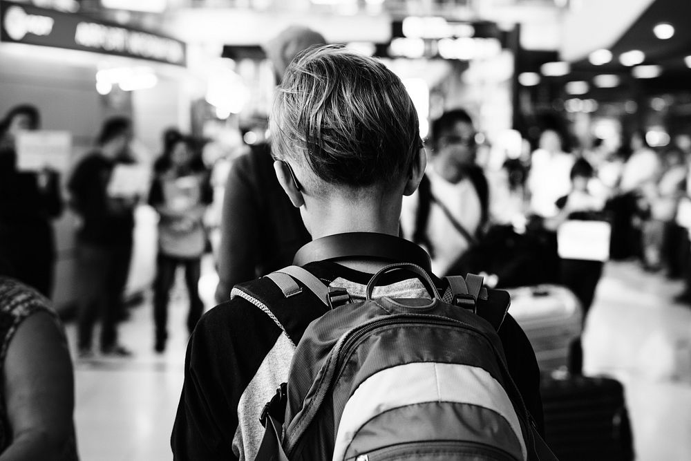 Rear view of young caucasian boy walking in the crowded at airport grayscale