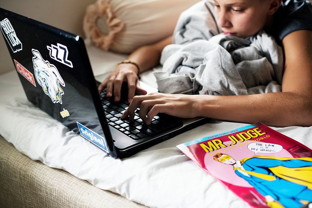 Closeup of young caucasian boy lying using computer laptop on bed