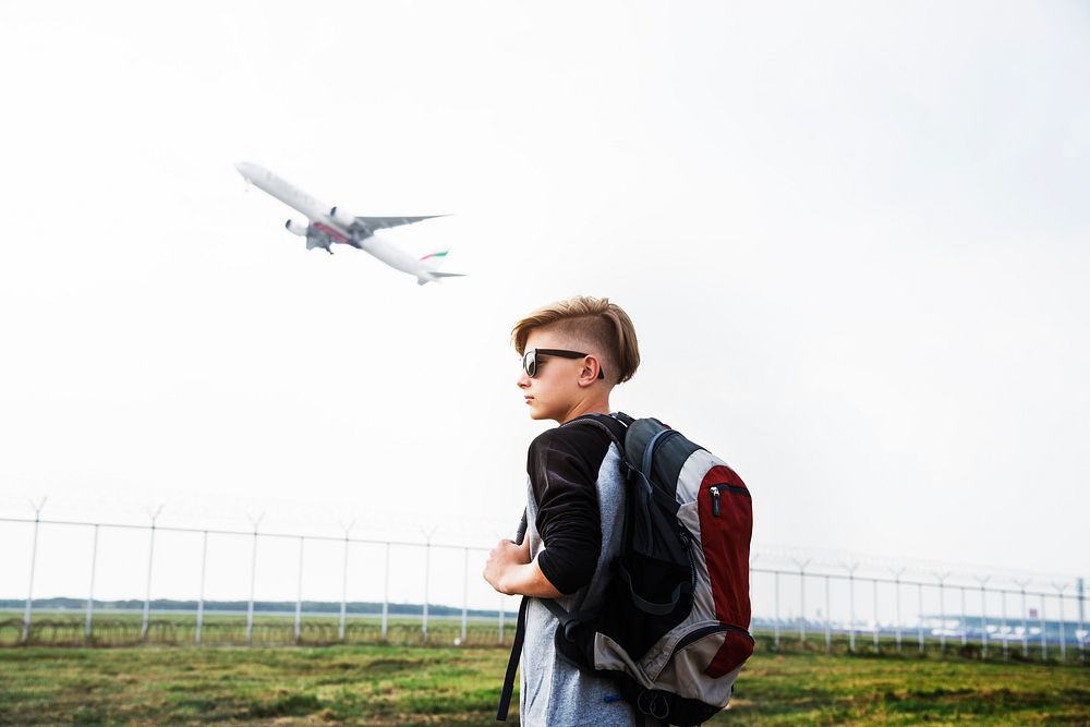 Young caucasian traveler standing outdoors with a takeoff airplane