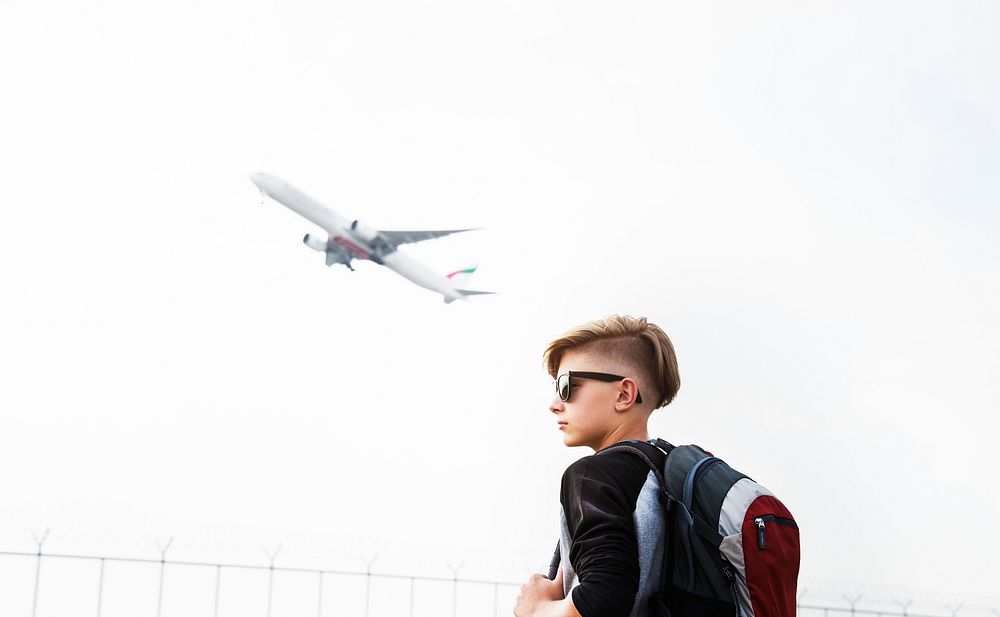 Young caucasian traveler standing outdoors with a takeoff airplane