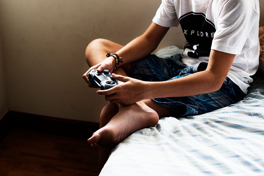 Young caucasian boy holding game control sitting on bed