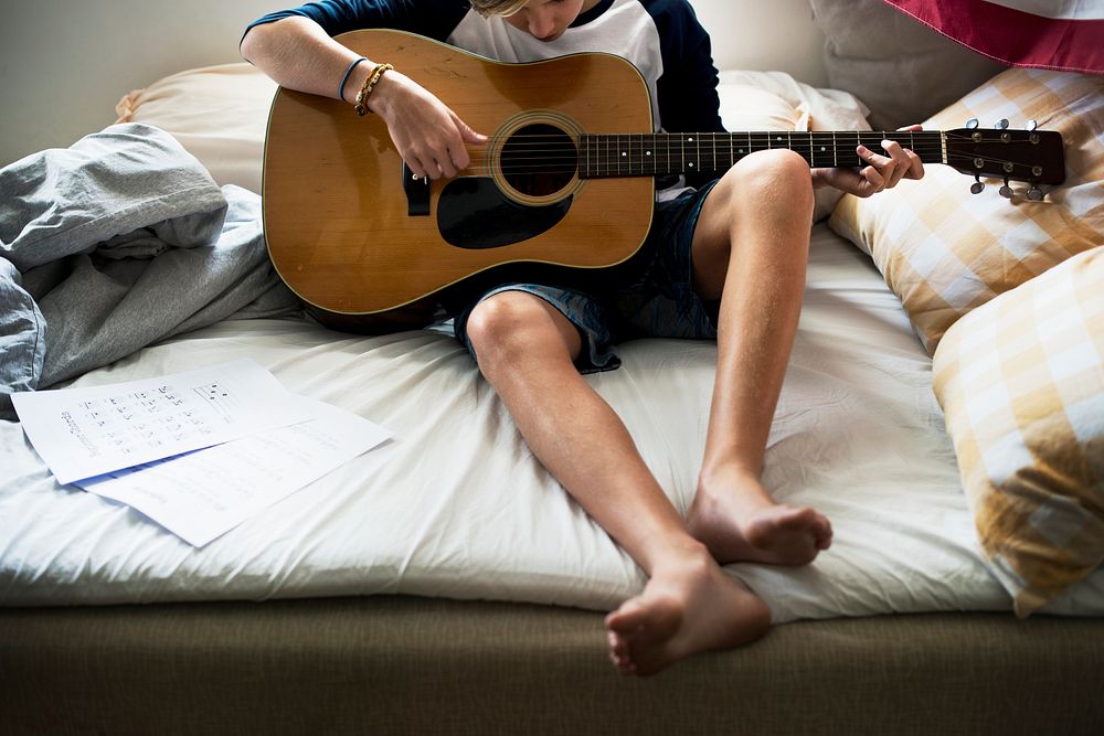 Closeup of young caucasian boy playing guitar on bed