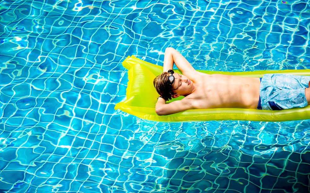 Young caucasian boy enjoying floating in the pool on pool inflatable bed