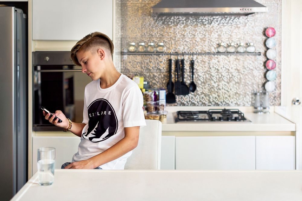 Young caucasian man sitting in the kitchen using mobile phone