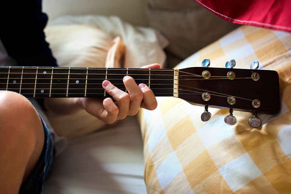 Closeup of young caucasian boy playing guitar on bed