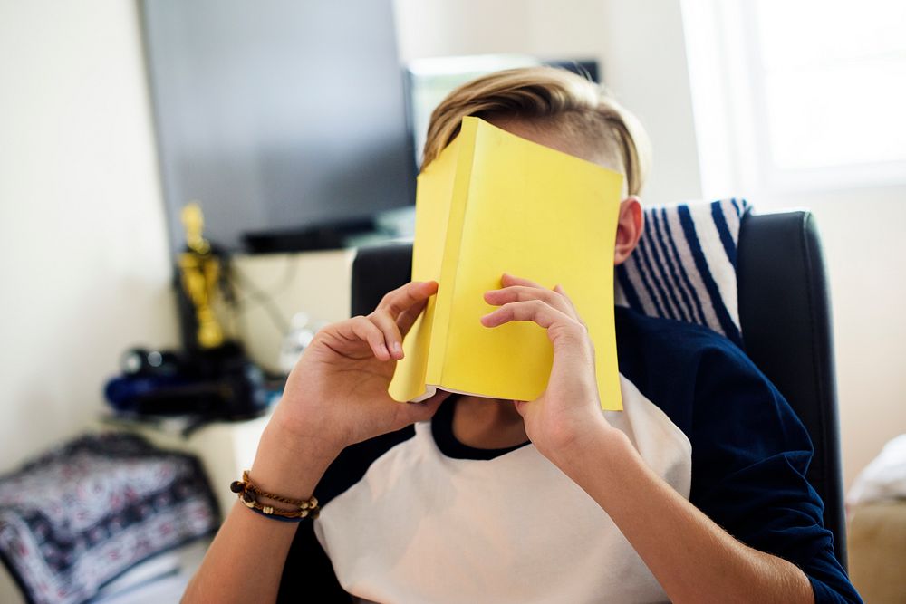 Young caucasian boy with yellow book covered face