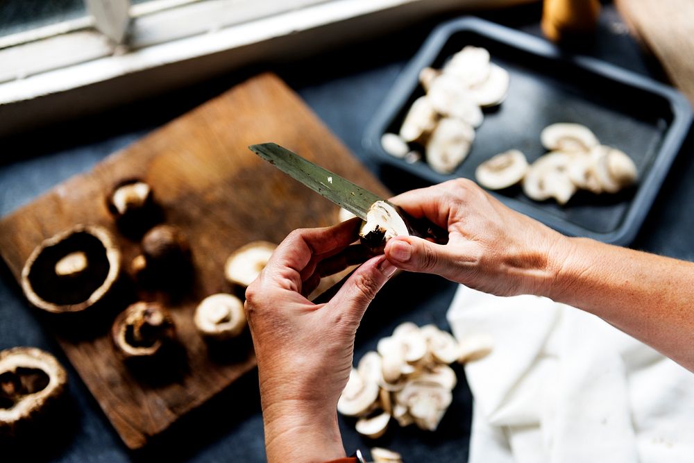 Closeup of hands with knife cutting mushroom